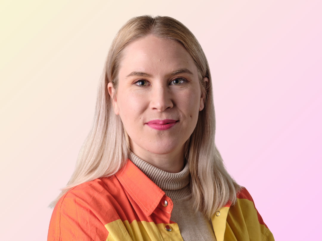 Emma Lindqvist poseeraa vaaleanpuna-keltaisen taustan edessä. Emmalla on päällä värikäs paita, jossa on punainen, keltainen ja vaaleanpunainen raita.